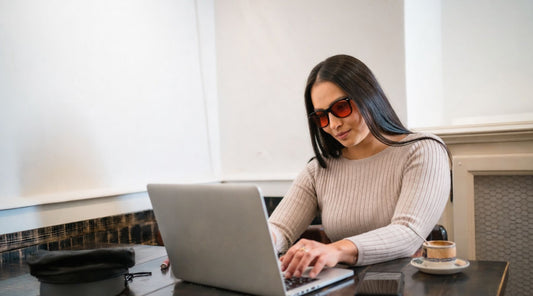 Woman wearing orange lens blue light blocking glasses before bed while working on a laptop in the evening